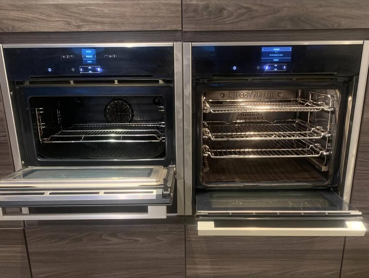 The same two ovens after cleaning, doors open, with clean interiors, clear door glass and the racks back in.