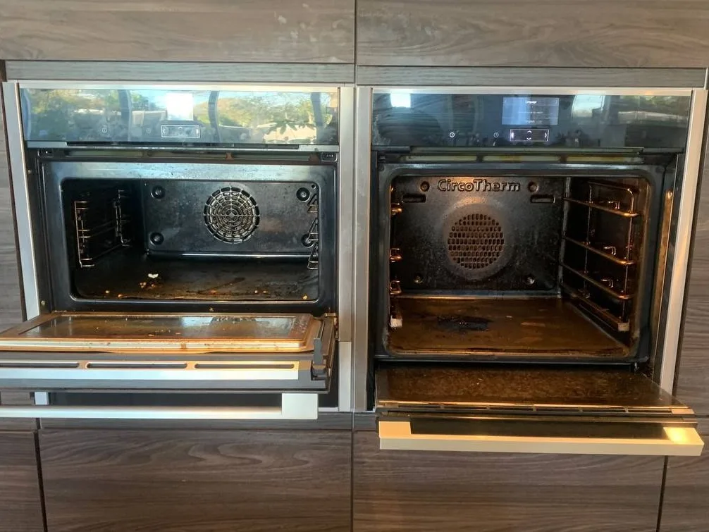 Two built-in ovens side by side in a dark wood kitchen unit before cleaning, doors open, with grease and burnt-on residue on the oven floors and the left-hand door glass.