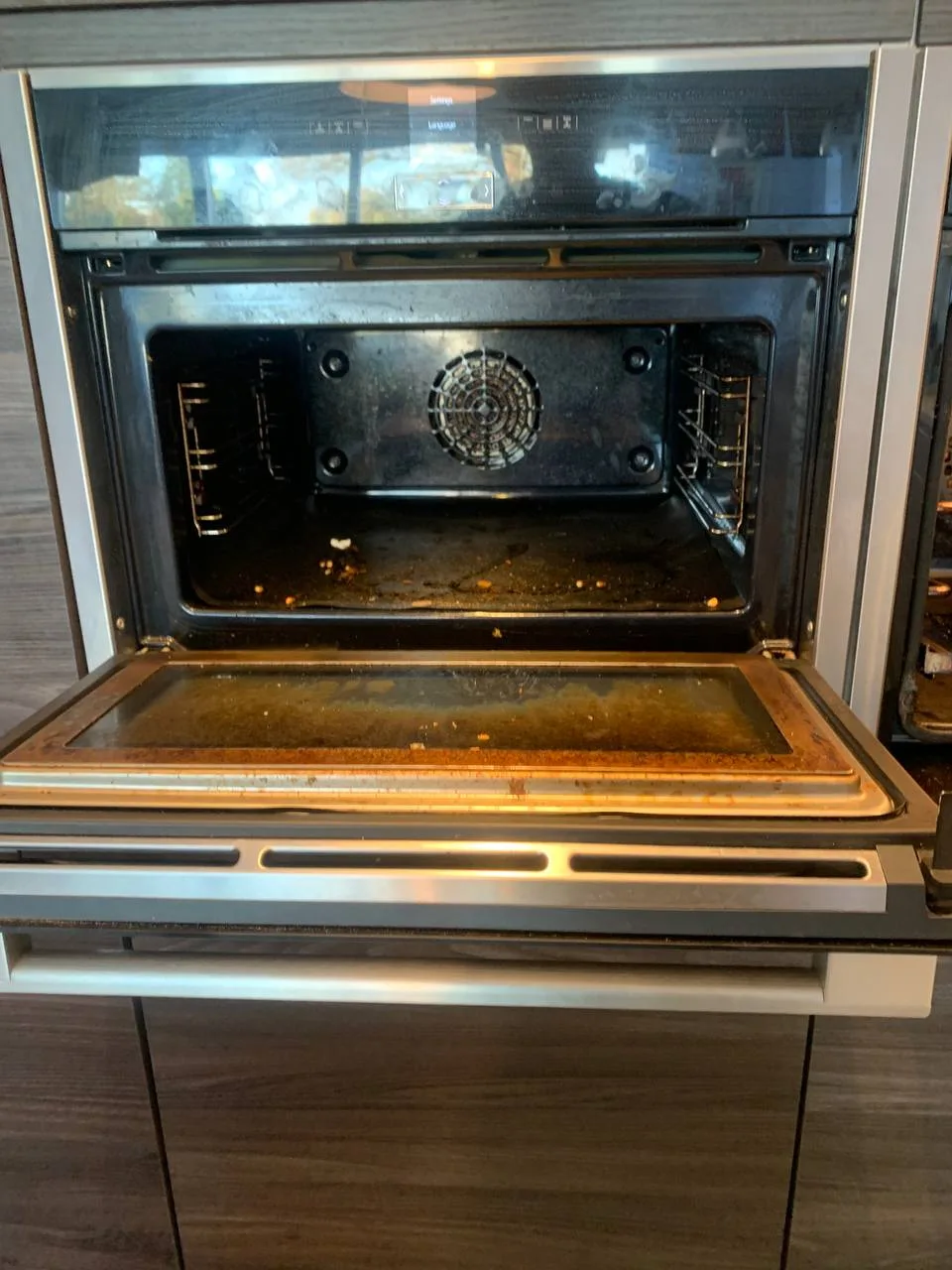The left-hand oven before cleaning, with brown baked-on grease on the inner door glass and dark staining inside.
