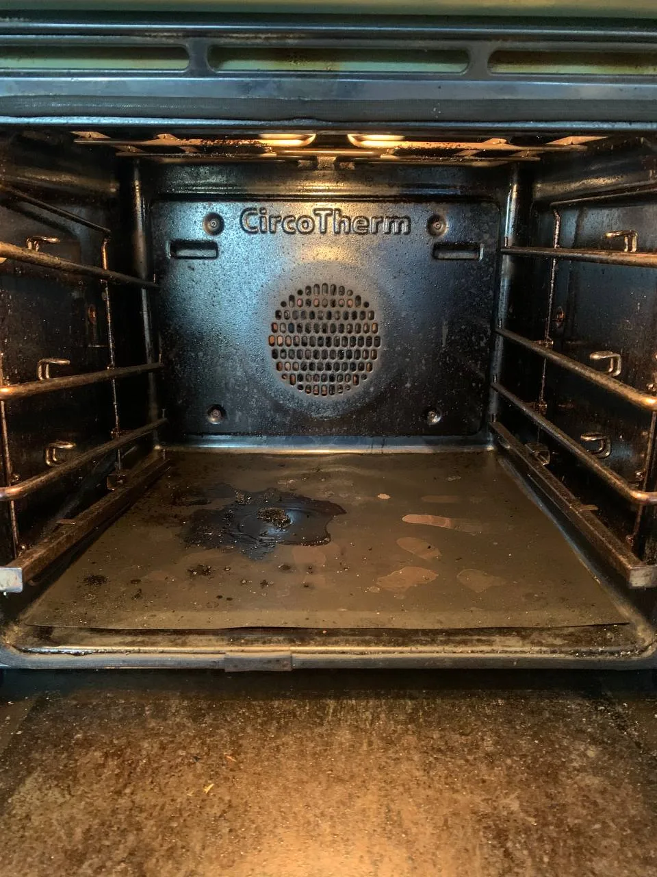Inside the right-hand oven before cleaning, with a burnt patch and grease on the floor and dark residue on the walls.