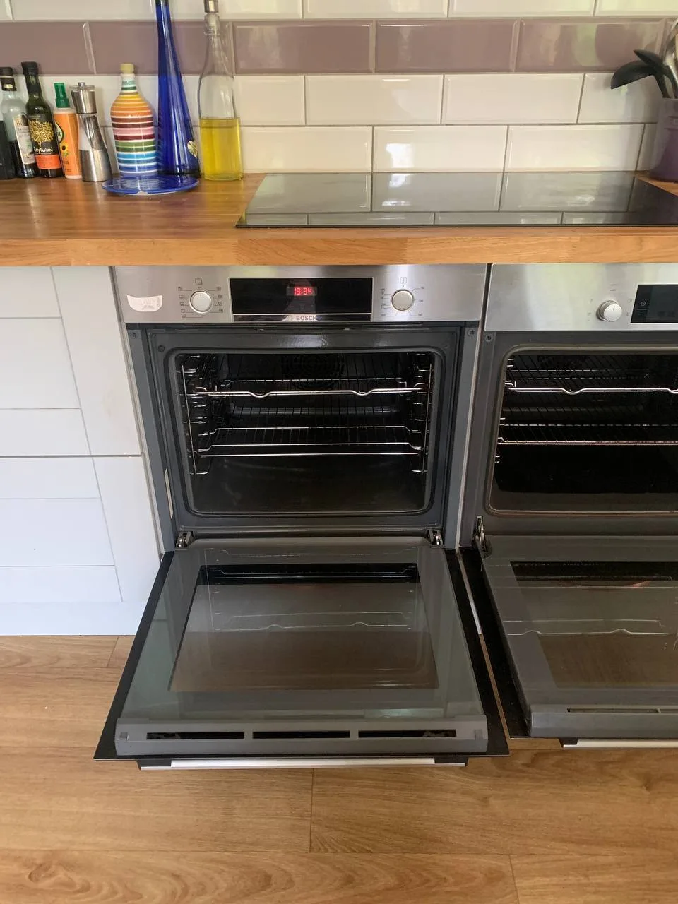 The same built-in oven after cleaning, door open, with clear glass and clean racks.