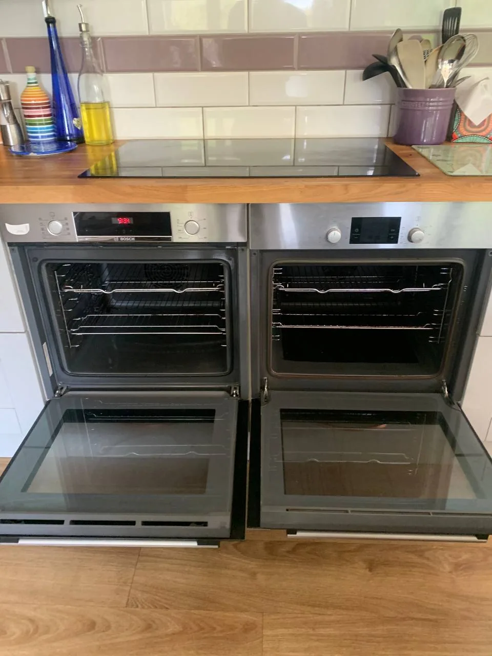 Two built-in ovens side by side after cleaning, both doors open, with clear glass and clean racks.