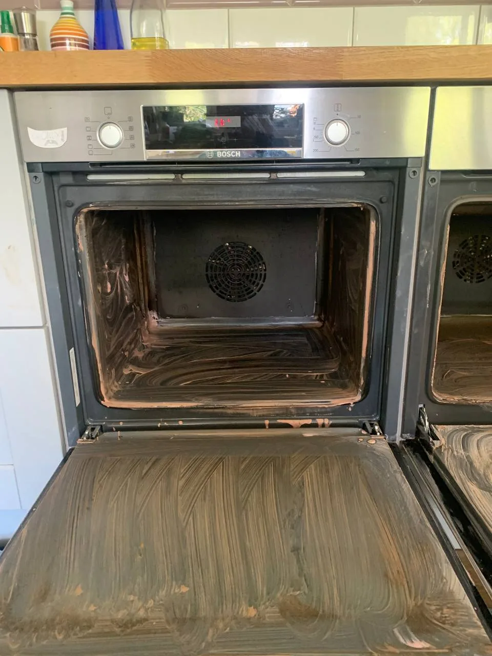 Built-in oven part-way through cleaning, with cleaning product spread over the inside of the cavity and over the open door.