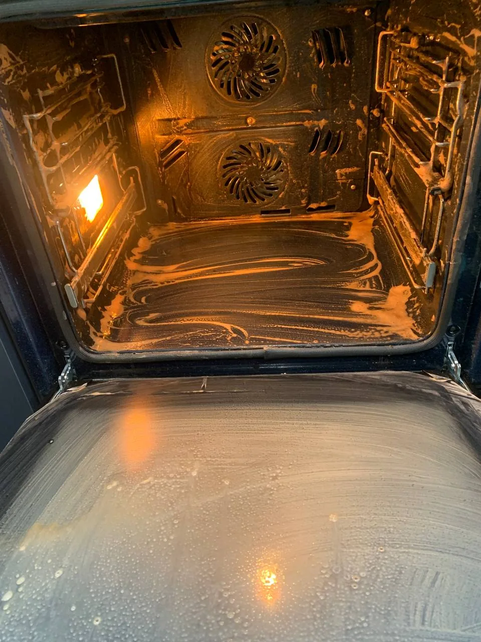 Oven interior lit from inside, coated with cleaning product.