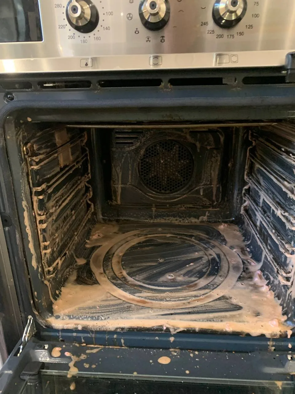 Oven interior with cleaning product on the walls and floor and the fan visible at the back.
