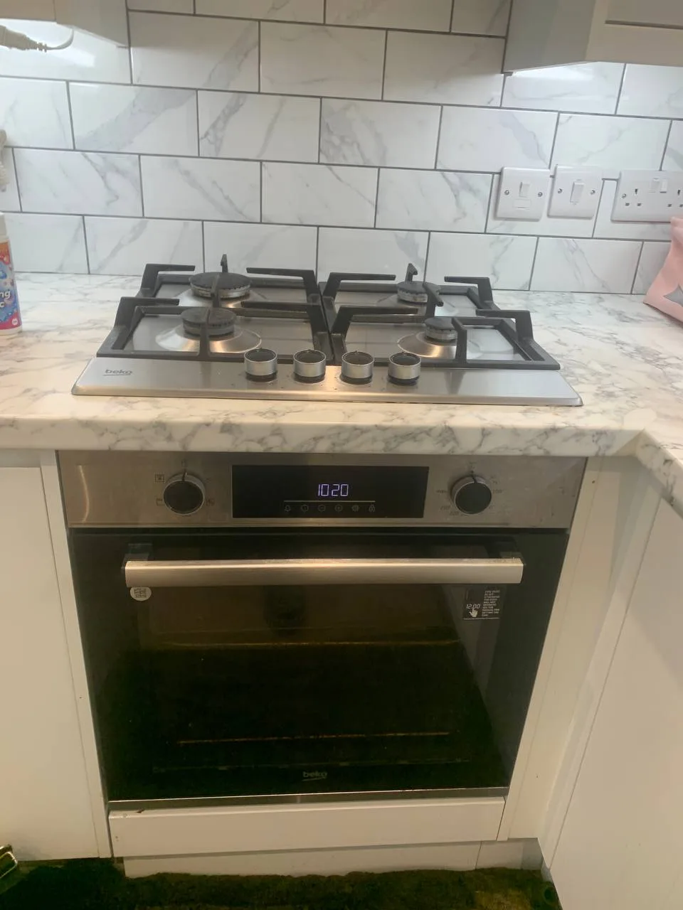 Built-in oven below a four-burner gas hob in a marble-effect kitchen.