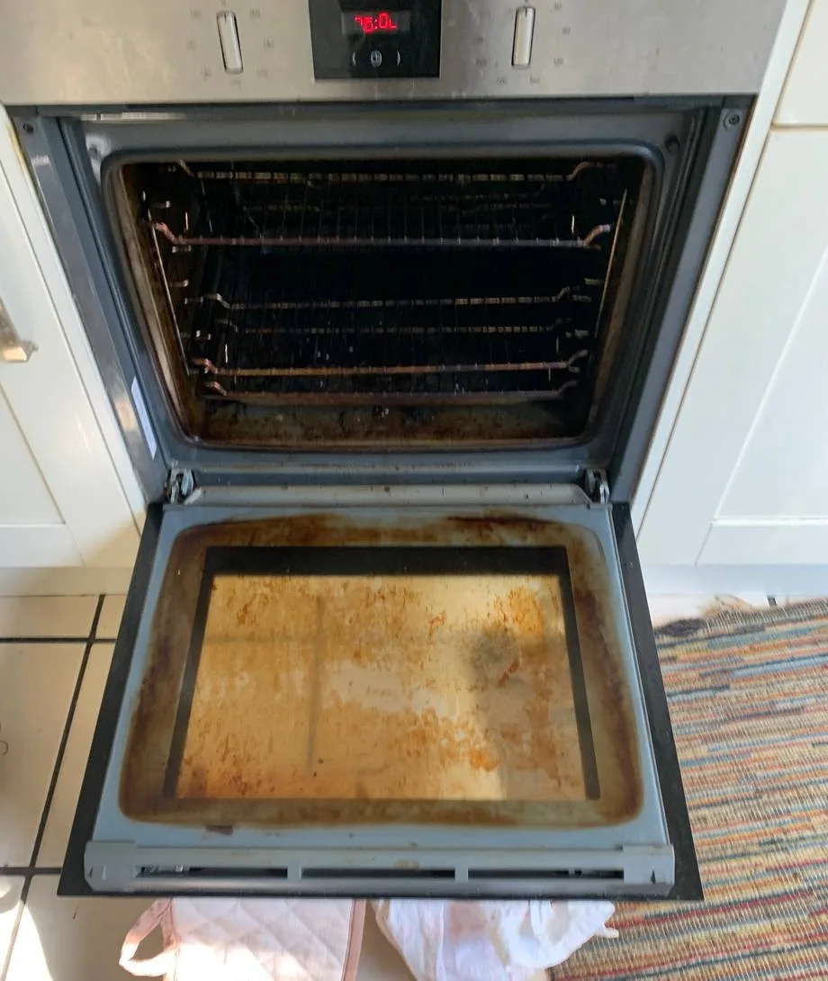 Oven door open, showing thick baked-on grease on the inner glass.