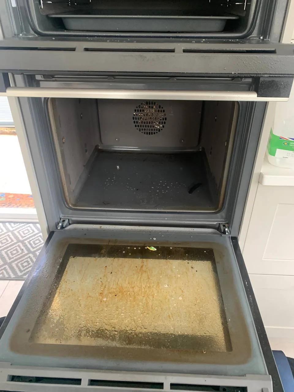Built-in oven with the door open, grease and burnt residue on the door glass and the floor of the oven.