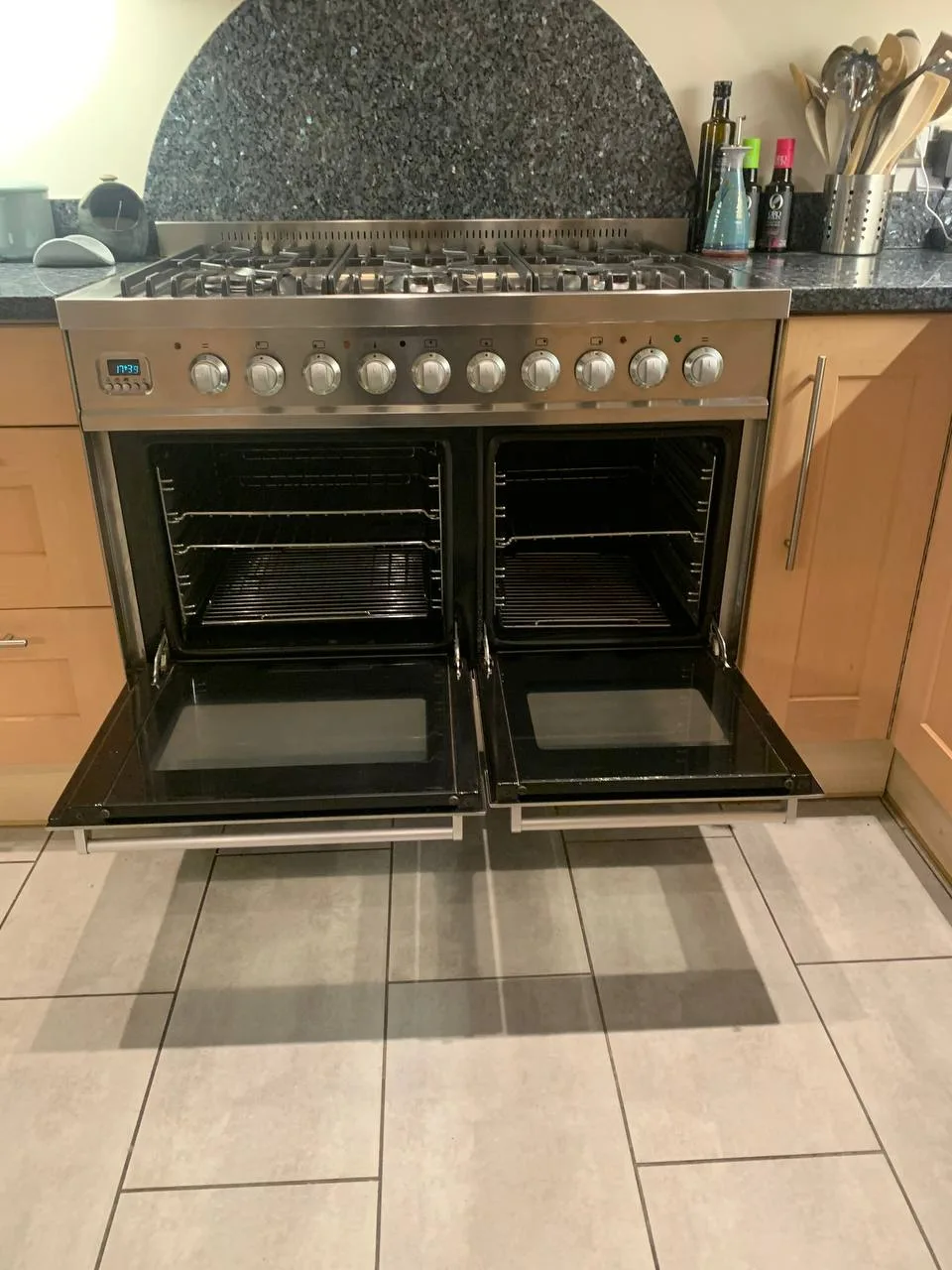 Stainless steel range cooker with both oven doors open, showing clean ovens and clear door glass.