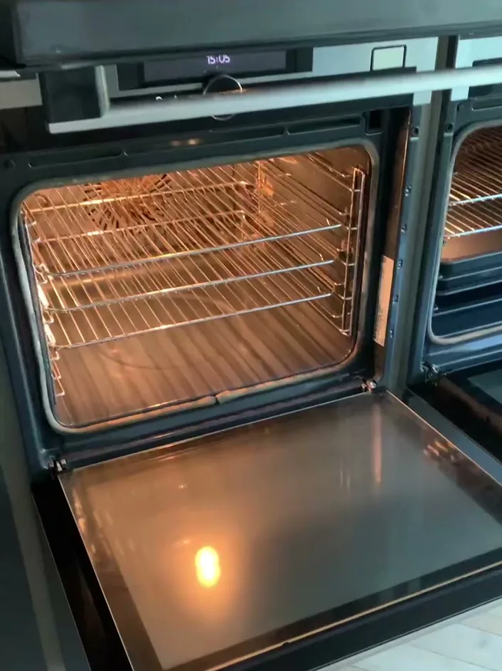 The same oven after cleaning, door open, with clear door glass and clean racks.