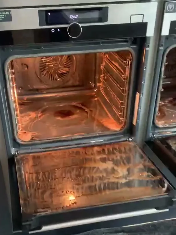 Built-in oven before cleaning, door open, with thick brown streaks of grease and cleaning product across the door glass and a stained oven floor.